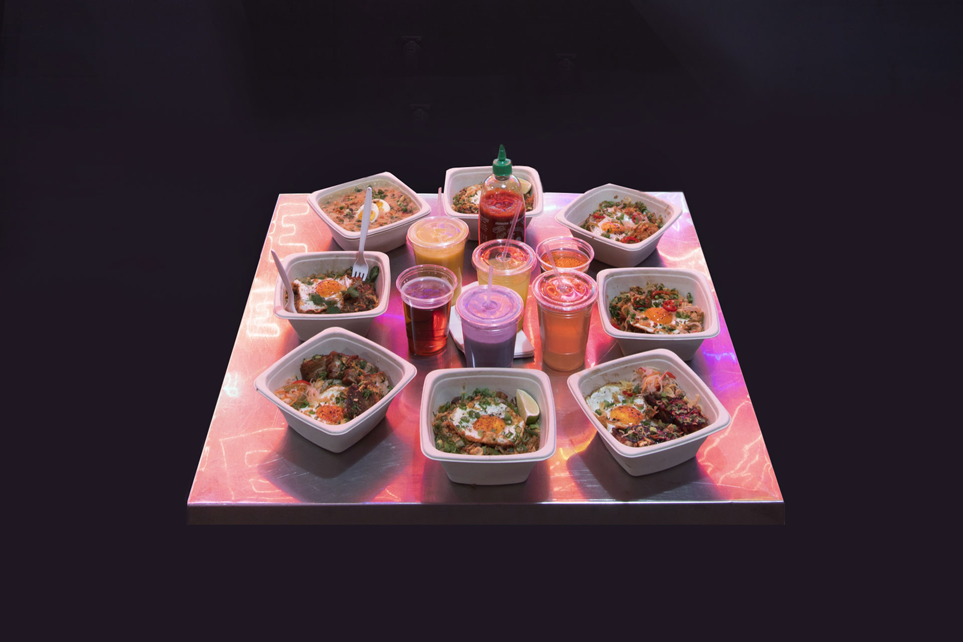 an assortment of sari sari store's full menu arranged on a stainless steal table reflecting the neon light from an art wall behind it